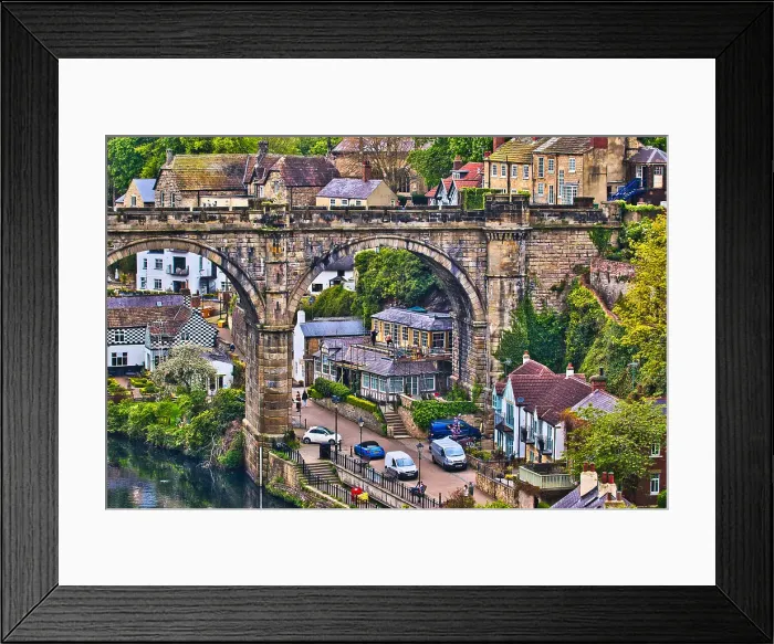 Framed Print : A picturesque view of a quaint village with an old stone bridge arching over a river, surrounded by lush greenery and traditional houses