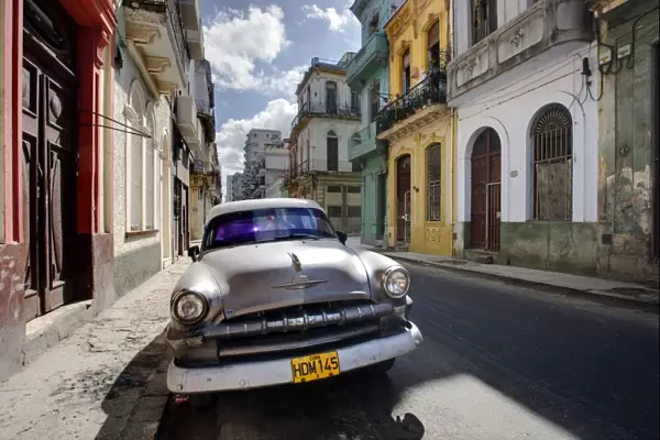 Old American Plymouth car parked on deserted street of old buildings, Havana Centro