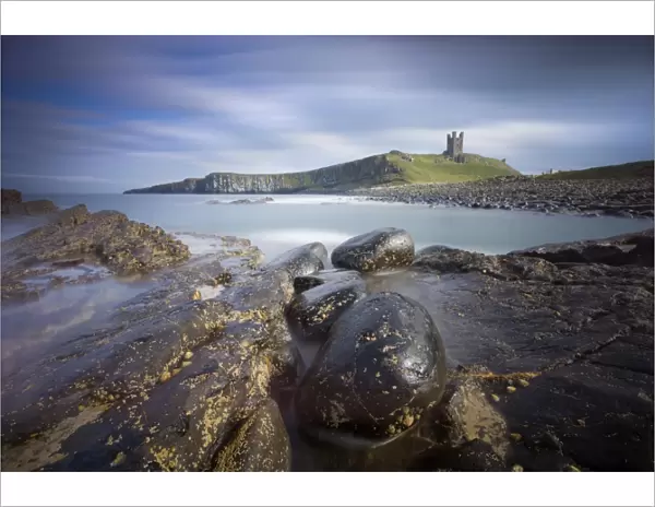 Dunstanburgh Castle bathed in afternoon sunlight with rocky coastline in foreground