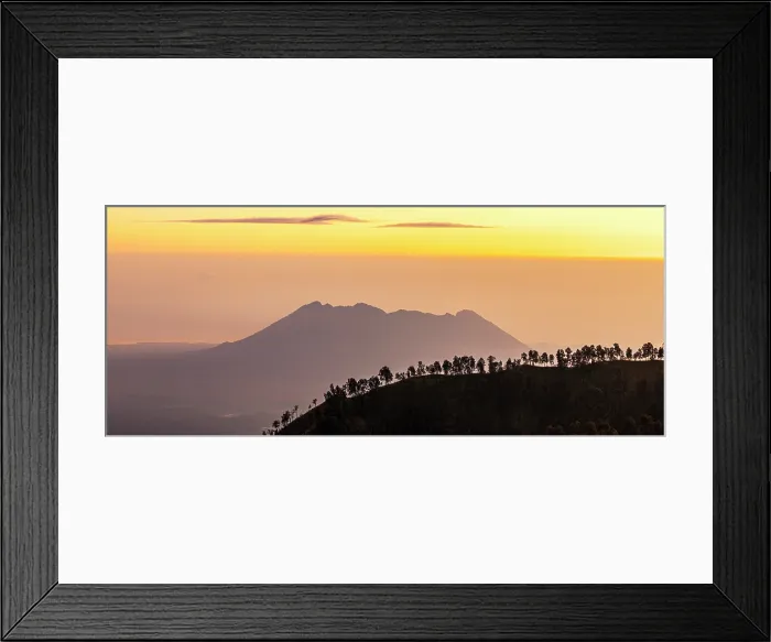 Framed Print : Foggy sunrise over silhouettes of trees on top of a mountain with volcano on background, Banyuwangi, East Java, Indonesia Framed Print : Foggy sunrise over silhouettes of trees on top of a mountain with volcano on background, Banyuwangi, East Java, Indonesia