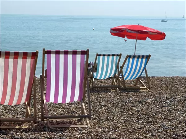 Coloured deck chairs on the pebble strand, Brighton, Sussex, England, United Kingdom