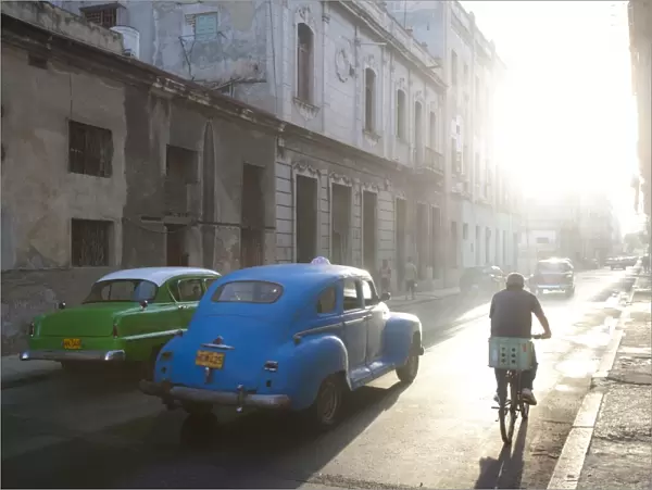 Street scene bathed in early morning sunlight showing old American cars and cyclists
