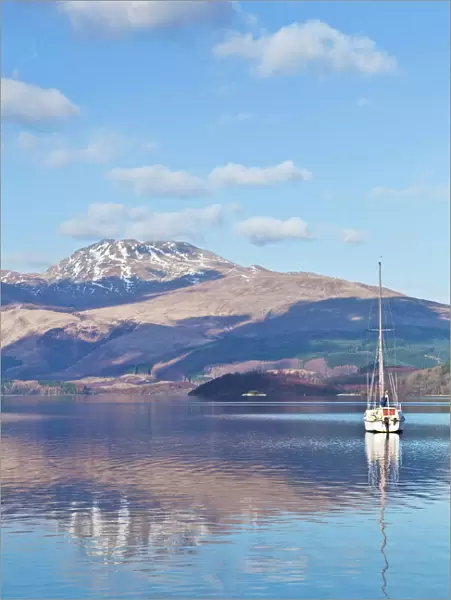 Picturesque tranquil Loch Lomond with sailing boat, snow covered Beinn Uird behind