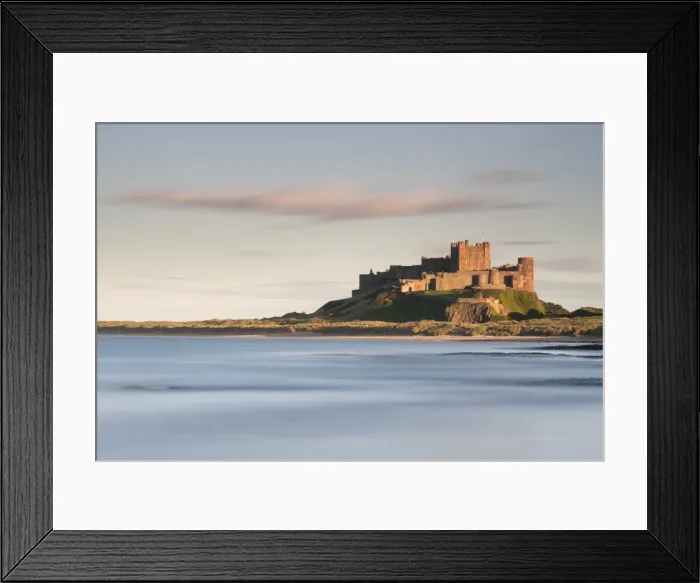 Framed Print : Bamburgh Castle bathed in golden evening light overlooking Bamburgh Bay with the sea filling the foreground, Northumberland, England, United