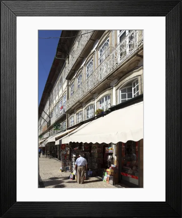 Framed Print : A newsagents stand under a building with a wrought iron balcony on the Largo do Toural Framed Print : A newsagents stand under a building with a wrought iron balcony on the Largo do Toural