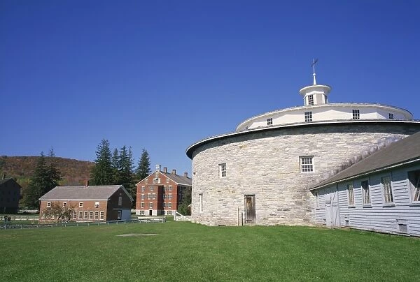 485-2874. Circular building with houses in the background at the Hancock Shaker Village