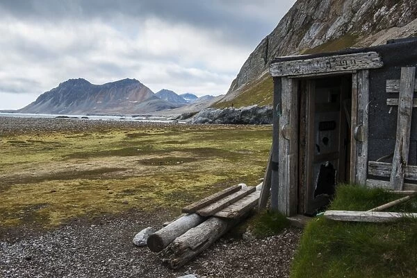 Abandoned hut on Alkhornet with a huge rock in the background, Svalbard, Arctic
