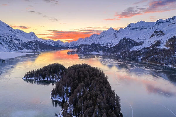 Aerial view of burning sky at sunset on frozen Lake Sils and snow capped mountains