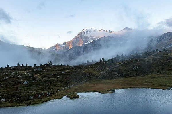 Aerial view of Fletschhorn and Galehorn mountains in fog at dawn from Hopschusee lake