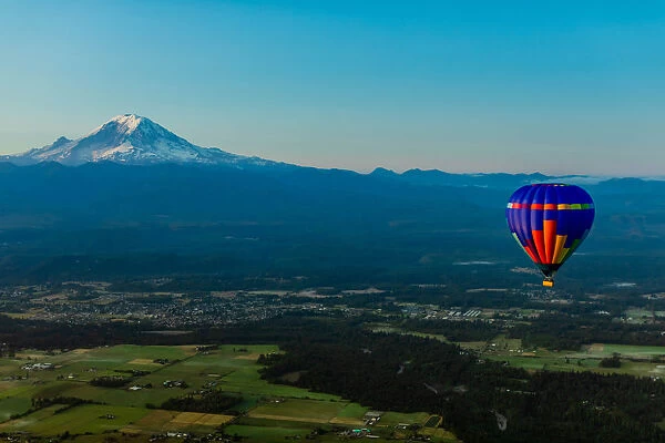 Aerial view of hot air balloon floating over farmland and Mount Rainier in the distance