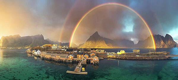 Aerial view of idyllic rainbows over Olstind mountain and fishermen cabins by the sea, Sakrisoy, Reine, Lofoten Islands, Nordland, Norway, Scandinavia, Europe