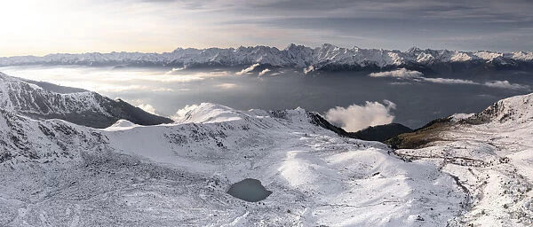 Aerial view of snowcapped Orobie Alps and Piani di Rhon emerging from autumn fog at dawn