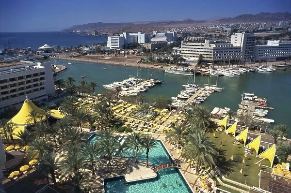 Aerial view over swimming pool, palm trees and the marina at Eilat, with modern buildings in the background, Israel