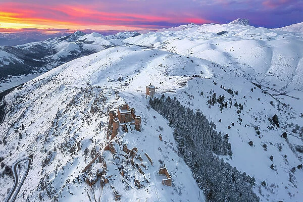 Aerial winter view of the snow covered Rocca Calascio castle and church of Santa Maria della Pieta, �with pink clouds at sunset, Rocca Calascio, Gran Sasso e Monti della Laga National Park, Campo Imperatore, L'Aquila province, Abruzzo, Italy