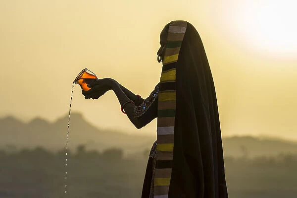 Ahir Woman in traditional colorful cloth pouring water at sunset, Great Rann of Kutch