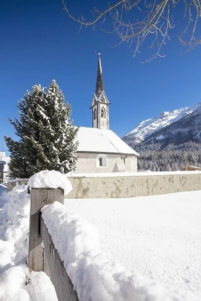 Alpine church covered with snow framed by blue sky, Cinuos, Canton of Graubunden