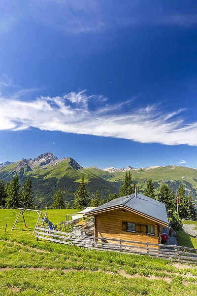 Alpine hut with Swiss flag, beneath stunning clouds. Surses, Surselva, Graubunden