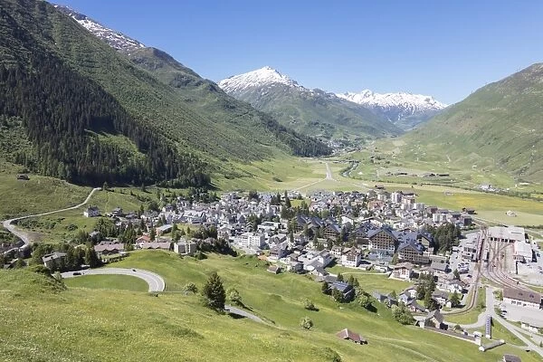 The alpine village of Andermatt surrounded by green meadows, and snowy peaks in the background
