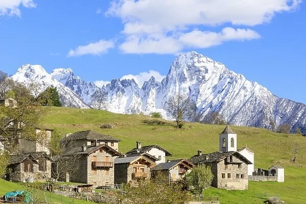 Alpine village and meadows framed by the snowy peak of Pizzo di Prata, Daloo, Chiavenna Valley