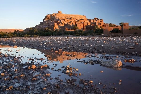 The ancient Kasbah Ait Benhaddou bathed in morning light and reflecting in river
