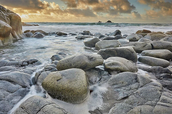 Atlantic rollers surge around shoreline granite boulders on a rising tide at sunset, Porth Nanven, a remote cove near St. Just, in the far west of Cornwall, England, United Kingdom, Europe