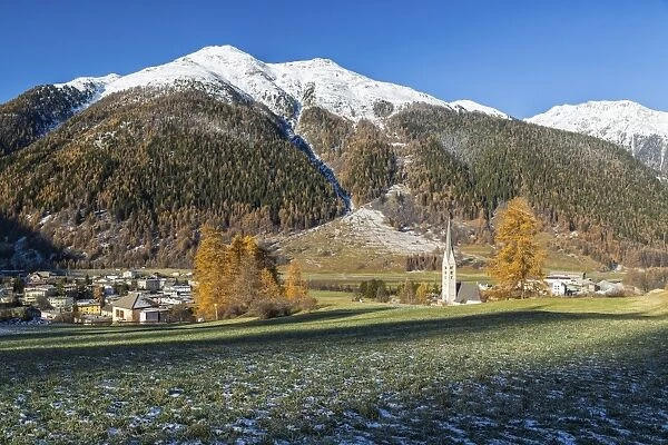 Autumn colors frame the village of Zernez surrounded by woods and snowy peaks, Engadine