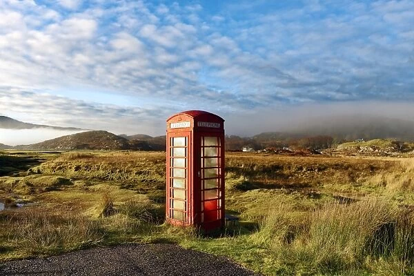 Autumn view of a red telephone box at the side of a quiet road in the remote misty
