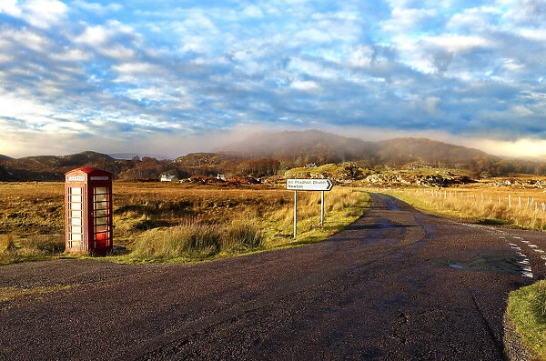 Autumn view of a red telephone box at the side of a quiet road in the remote misty