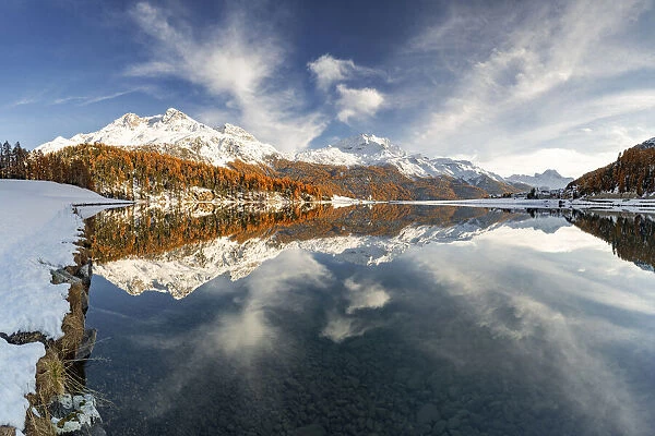 Autumn woods and snowcapped mountains mirrored in the clear water of Champfer lake at