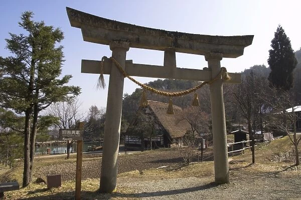 Backlit Shinto torii with traditional house beyond