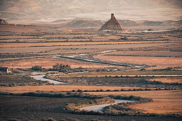 The badlands of Bardenas Reales at sunrise with a winding road leading towards the Castildetierra rock formation, Navarre, Spain, Europe