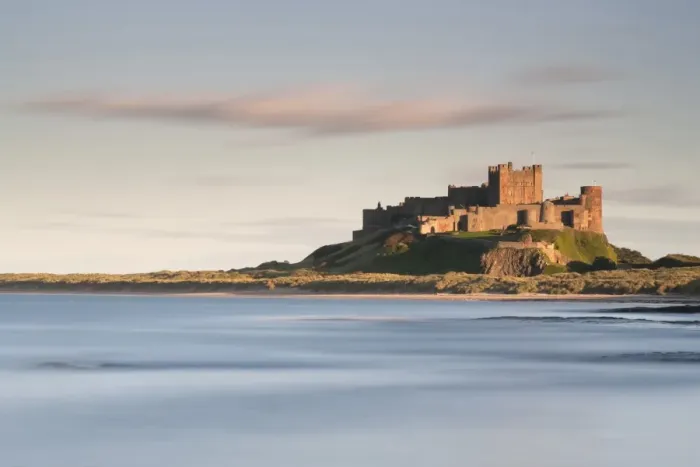 Framed Print : Bamburgh Castle bathed in golden evening light overlooking Bamburgh Bay with the sea filling the foreground, Northumberland, England, United