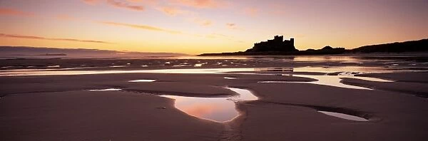 Bamburgh castle in silhouette at sunrise, with rock pools on empty beach