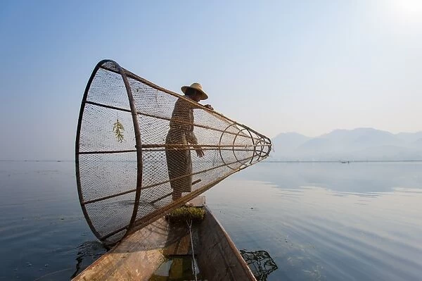 A basket fisherman on Inle Lake prepares to plunge his cone shaped net, Shan State