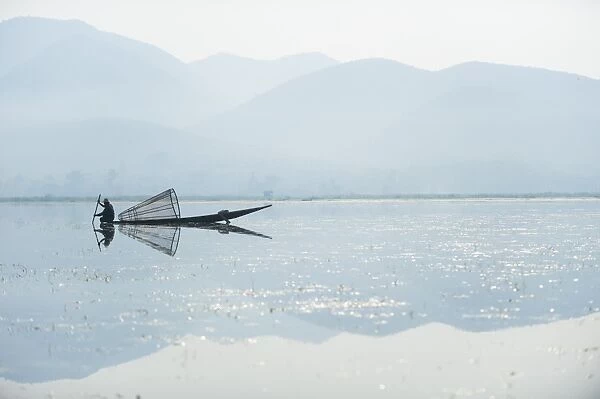 A basket fisherman on Inle Lake scans the still and shallow water for signs of life
