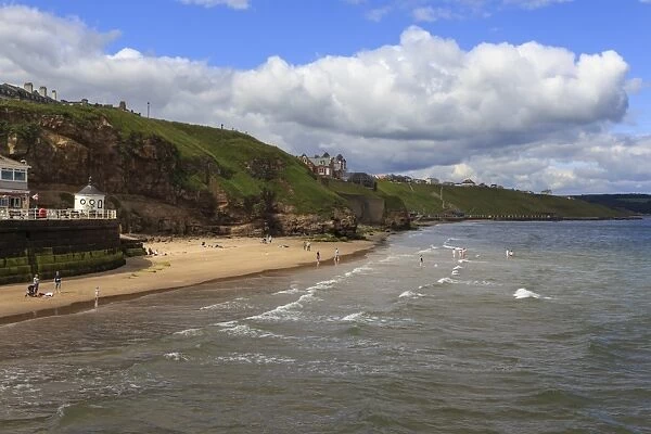 Bathers on West Cliff Beach, backed by grassy cliffs in summer, Whitby, North Yorkshire