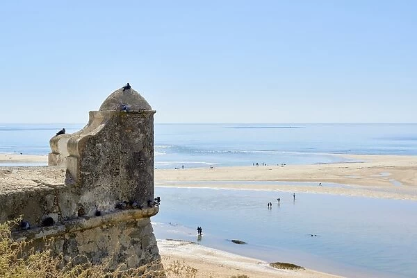 Beachgoers crossing a lagoon formed by the low tide, and detail of a watchtower in Cacela Velha