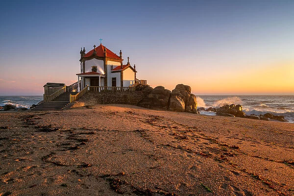 Beautiful chapel of Capela do Senhor da Pedra on the beach at sunset in Miramar