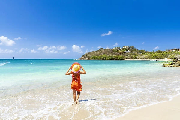 Beautiful woman with orange dress and straw hat standing on a tropical beach, Antigua, West Indies, Caribbean, Central America