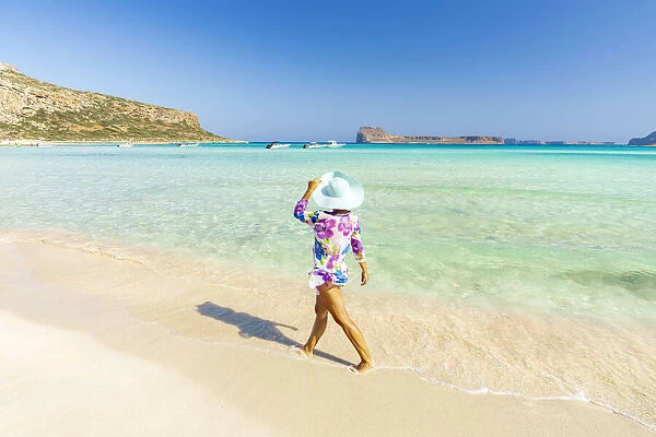 Beautiful woman with sun hat walking on idyllic empty beach, Crete, Greek Islands, Greece