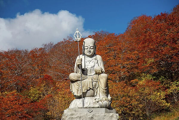 Big shizo statue in front of fire red autumnal leaves at beautiful Japanese temple surrounded by autumn colors, Osorezan Bodaiji Temple, Mutsu, Aomori prefecture, Honshu, Japan, Asia