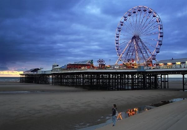 Big wheel and amusements on Central Pier at sunset with young women looking on, Blackpool