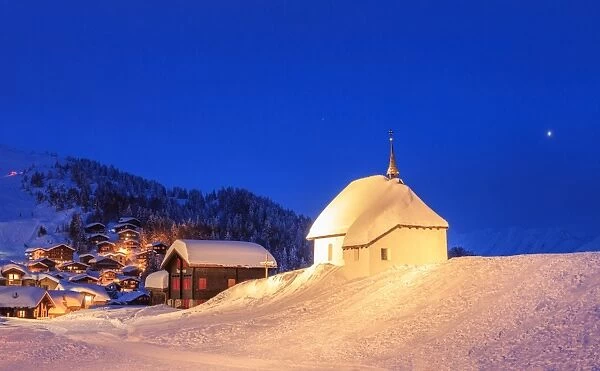 Blue dusk on the alpine village and church covered with snow, Bettmeralp, district of Raron