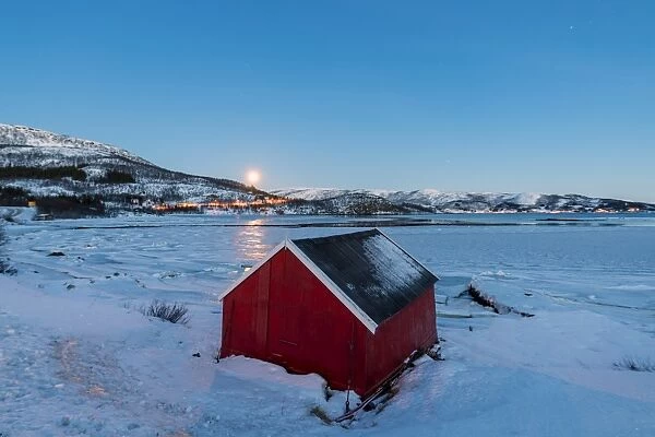 The blue light of dusk on the typical house of fishermen framed by the frozen sea