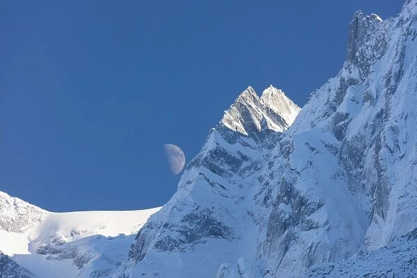 Blue sky and moon on the snowy ridges of the high peaks, Soglio, Bregaglia Valley
