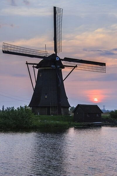 Blue sky and pink clouds on the windmill reflected in the canal at dawn, Kinderdijk