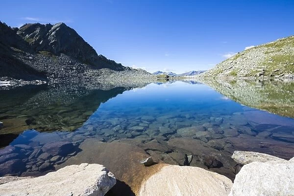 Blue sky and rocky peaks reflected in the blue Lago Nero, Chiavenna Valley, Valtellina