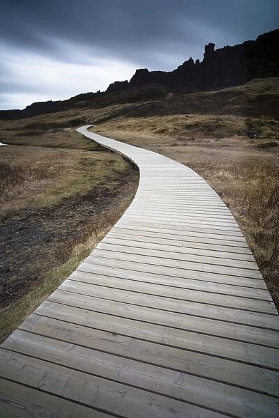 Boardwalk meandering towards rugged cliffs and stormy sky at Thingvellir National Park near Reykjavik, Iceland
