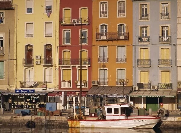 Boat, buildings with balconies and shops beneath on the waterfront, Sete