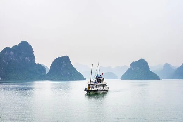 A boat passes through foggy karst landscape in Ha Long Bay, Quang Ninh Province, Vietnam